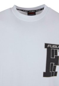 Balta kokvilnas T-krekls ar lielu melnu grafisko logo kreisajā krūtī. Apaļš dekoltē ar kontrastējošu drukātu etiķeti iekšpusē.