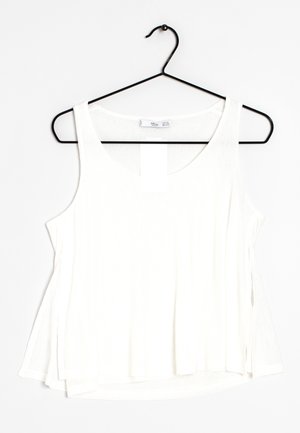 Haut blanc sans manches ample suspendu sur un cintre métallique noir sur fond blanc.