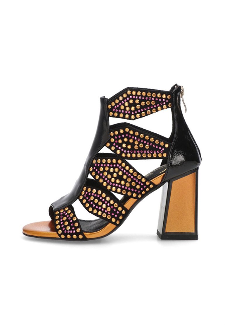 Sandalia negra de tacón alto con diseño abierto, recortes geométricos, adornos de tachuelas doradas y rosas, y un fuerte tacón cuadrado.