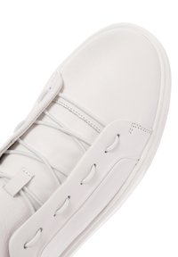 Zapatilla de piel blanca con acabado suave, cordones planos y diseño minimalista. Presenta detalles de costura y una forma de punta redondeada.