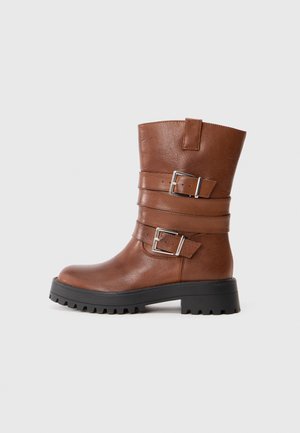Brown leather ankle boot with two adjustable buckles, rounded toe, and a chunky black rubber sole featuring a textured tread for grip.