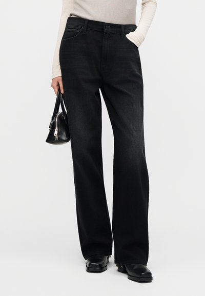 Μαύρο τζιν με ίσια γραμμή στο πόδι, που διαθέτει κλασικό στυλ με πέντε τσέπες και διακριτή υφή. Συνδυάζεται με μια μικρή μαύρη τσάντα χειρός.