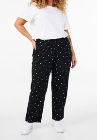 Svarta prickiga byxor med elastisk midja och sidfickor, tillsammans med en enkel vit t-shirt och vita sneakers.