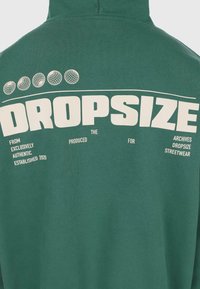 Sweat à capuche vert foncé avec le texte blanc "DROPSIZE" et de petites icônes de globe au-dessus, accompagnés de phrases de marque supplémentaires sous le texte principal.
