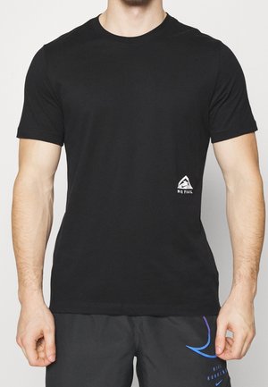 Mann trägt ein schwarzes kurzärmeliges Nike Trail T-Shirt und schwarze Nike Laufshorts mit blauen und violetten Akzenten.