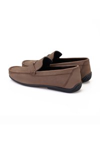 Braune Wildlederslipper mit schwarzen Gummisohlen, genähten Details und einer Klappe über der Zunge. Glatte Textur und rundes Zehendesign.
