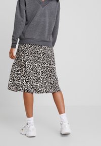 Sweater gris con escote en forma de V, combinado con una falda crema hasta la rodilla con un estampado de leopardo negro. Zapatillas blancas y calcetines acanalados.
