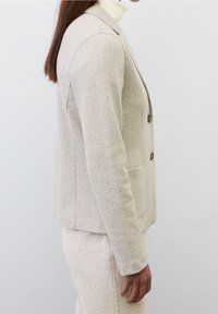 Beige herringbone blejzr s přiléhavým střihem, klopami, dvěma knoflíky a bočními kapsami, spárovaný s odpovídajícími kalhotami.