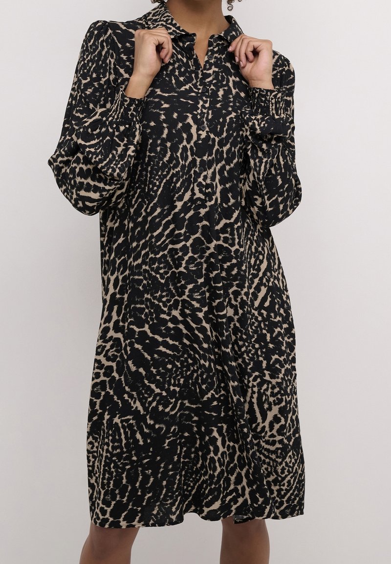 Robe chemise à manches longues à imprimé léopard noir et beige, avec boutonnage sur le devant et coupe décontractée. Le tissu a une texture lisse.