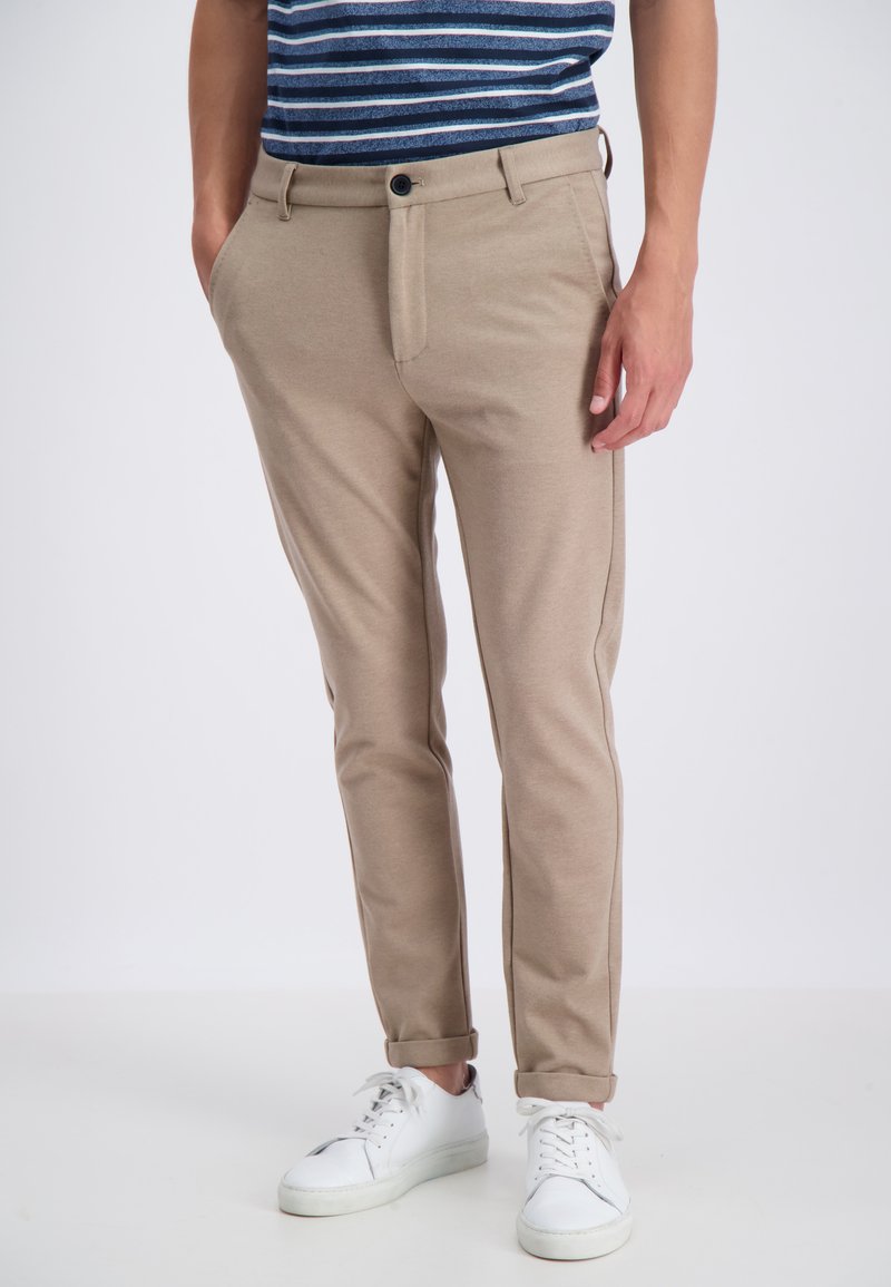 Beige trousers with a tailored fit, featuring a buttoned fly and side pockets. Worn with a striped shirt and white sneakers.