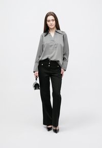 Gray long-sleeve blouse with a collar, paired with high-waisted black trousers featuring gold button accents and sleek black heels.