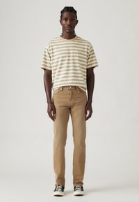 T-shirt rayé en coton beige et blanc, associé à un jean marron clair. Présente une coupe décontractée, des manches courtes et des baskets noires.