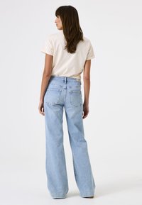 Helle blaue weit geschnittene Jeans mit hoher Taille, kombiniert mit einem weichen beigen T-Shirt. Die Jeans haben zwei Hintertaschen und ein schlichtes Design.