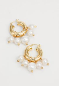 Orecchini a cerchio color oro con diverse perle bianche appese, con superfici metalliche lisce e dettagli in filo. Misurano circa 3 cm di diametro.