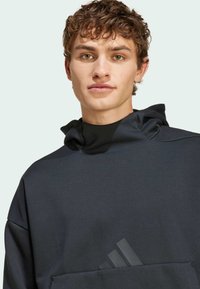 Black pullover hoodie made of soft fabric, featuring a high collar, front pocket, and tonal three-stripe logo accent on the front.
