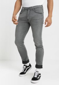 Šedé džíny s úzkým střihem, s klasickým pětipocket designem, ohrnutými lemy a kombinované s černými teniskami.