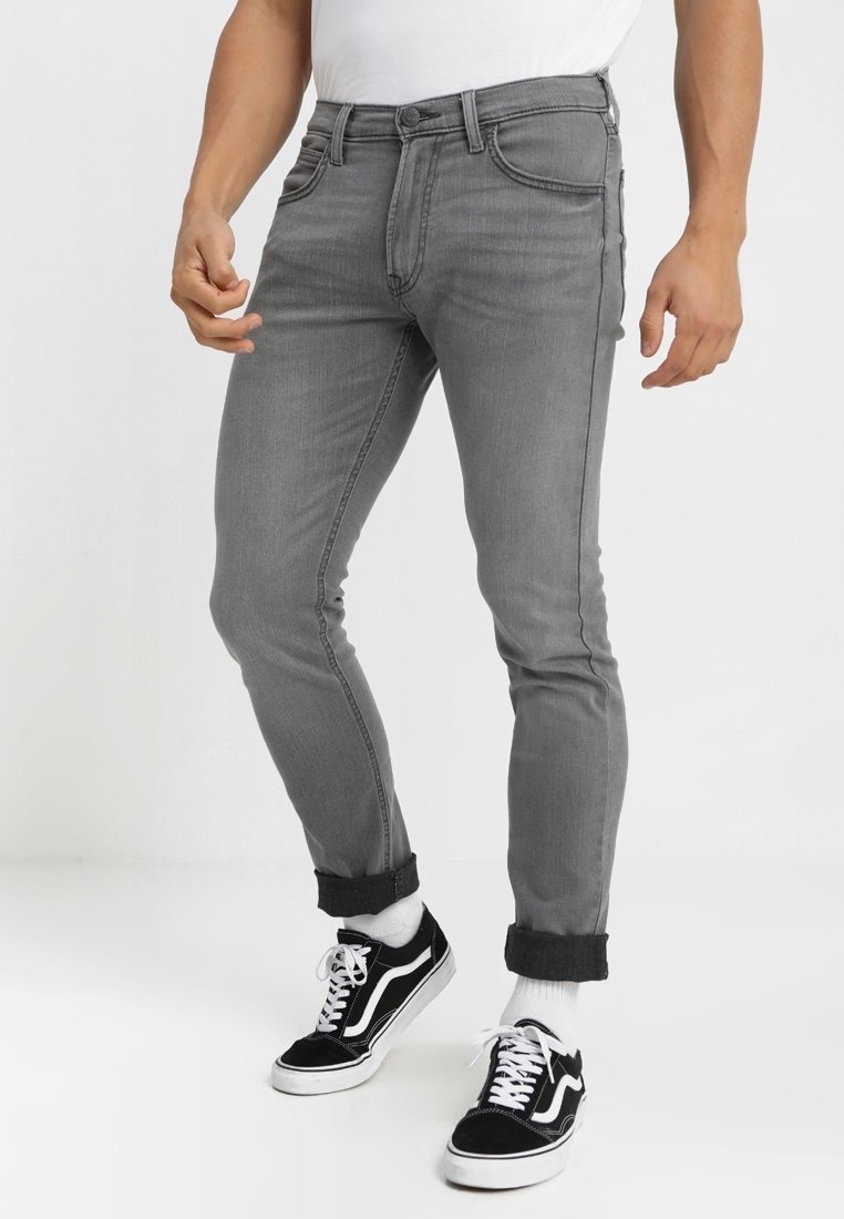 Šedé džíny s úzkým střihem, s klasickým pětipocket designem, ohrnutými lemy a kombinované s černými teniskami.