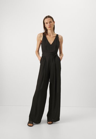 Svart ermeløs jumpsuit med V-hals, innsnevring i midjen og vid buksestil, med sidelommer og en glatt tekstur.