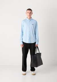 Lyseblå skjorte med lange ermer og knapp design, svart "BOSS" logo, svarte bukser, hvite sneakers og en stor svart totebag.