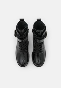 Bottes de cheville en cuir verni noir avec un bout rond, lacets à l'avant, sangle à boucle réglable et finition texturée, vues de dessus.