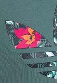 Grön plagg med lager av geometriska och blommönster i svart, turkos och orange. Ribbad yta med flera designelement.