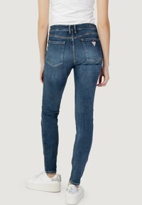 Tynne blå denimjeans med høy midje, med et klassisk fem-lomme design og subtil søm, parret med hvite sneakers.