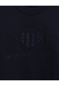 Marinblå sweatshirt med upphöjd brodering av "GANT"-logotypen och "AMERICAN SPORTSWEAR," strukturerad tygkvalitet, rund halsringning.