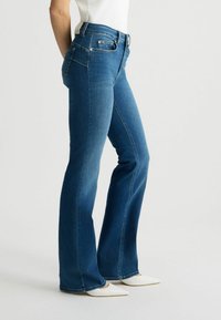 Laienevad sinised denim püksid kõrge vöökohtadega, esitaskute ja hõbedaste detailidega. Sile tekstuur kerge pleekimisega.