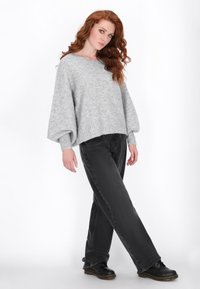 Grauer, übergroßer Strickpullover mit gerippten Bündchen und Saum, kombiniert mit dunkelgrauen, geraden Jeans und schwarzen, schnürbaren Schuhen.