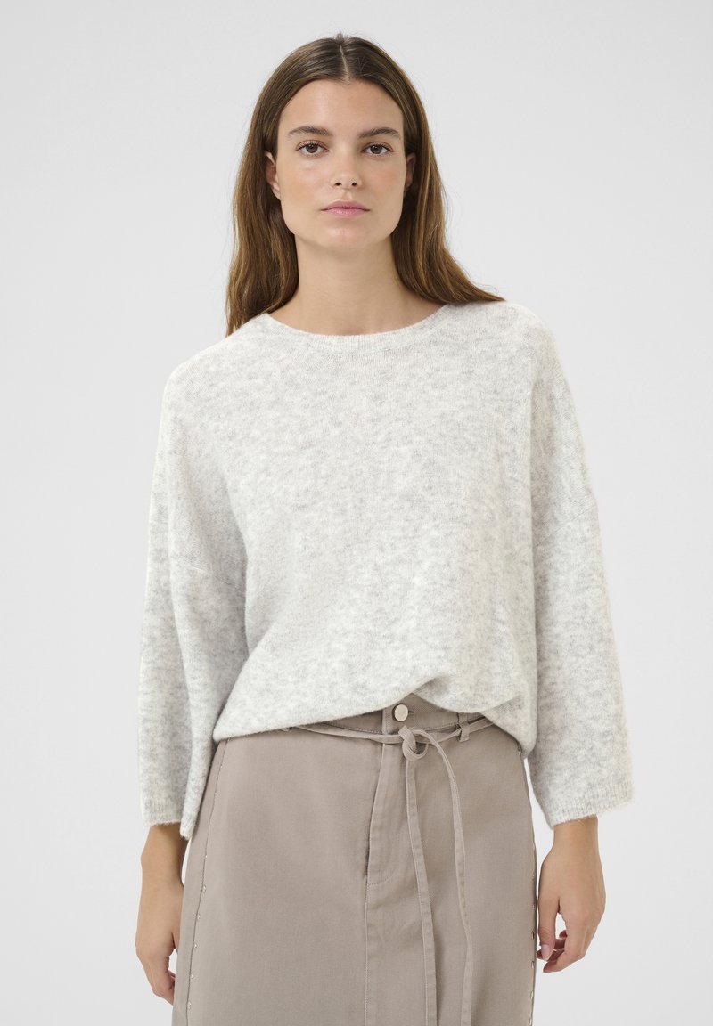 Lichtgrijze gebreide trui met een ronde halslijn en lange, losse mouwen, gecombineerd met een taupe rok met een strik taille en zijknopen.