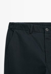 Pantalons bleu marine foncé en coton, avec une texture lisse, une taille plate, des poches latérales et une fermeture à bouton avec passants de ceinture.