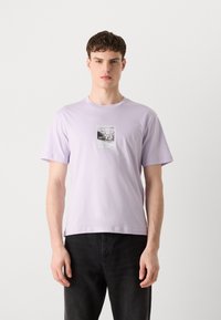 Light lavender cotton t-shirt featuring a front graphic print with a black and white photo and red text accents. The design has a classic fit.
