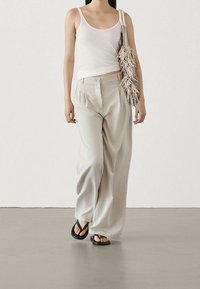 Light beige, flowy wide-leg trousers with a high waist, paired with a fitted white tank top. Black flip-flops and a fringed purse complete the look.