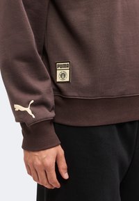 Καφέ μανίκι φούτερ και μέση με μπεζ λογότυπο Puma στη μανσέτα και ορθογώνιο πέτο Puma και FC St. Pauli 1910 κοντά στη μέση.