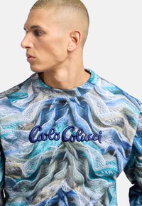 Sudadera de cuello redondo con un patrón de punto multicolor que presenta tonos de azul y verde, con "Carlo Colucci" bordado en azul oscuro.