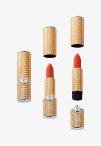 Des tubes à lèvres dorés et noirs présentent un design en maille texturée, avec trois tubes fermés et deux affichant des rouges à lèvres rouges vifs.