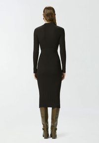 Vestido negro acanalado con mangas largas, silueta ajustada, longitud por la mitad de la pantorrilla, combinado con botas verde oliva hasta la rodilla.