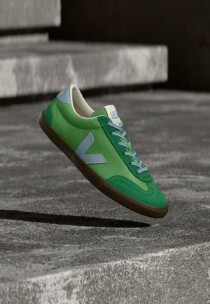 Groene leren sneaker met blauwe accenten, gestructureerde buitenzool en lichtblauwe veters. Heeft een retrovorm en een logo aan de zijkant.