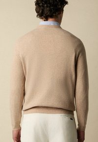 Maglione beige a girocollo con finitura testurizzata, polsini e orlo a costine. Indossato sopra una camicia colletto azzurro per uno stile a strati.
