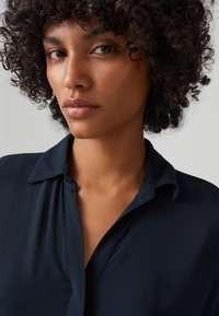 Blusa di seta blu navy con colletto e bottoni. Caratterizzata da una consistenza morbida e liscia e una vestibilità rilassata, presenta un design semplice ed elegante.