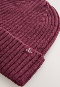 Maroon knitted beanie with vertical ribbing. Features a folded cuff with a small white logo tag. Soft texture and snug fit.