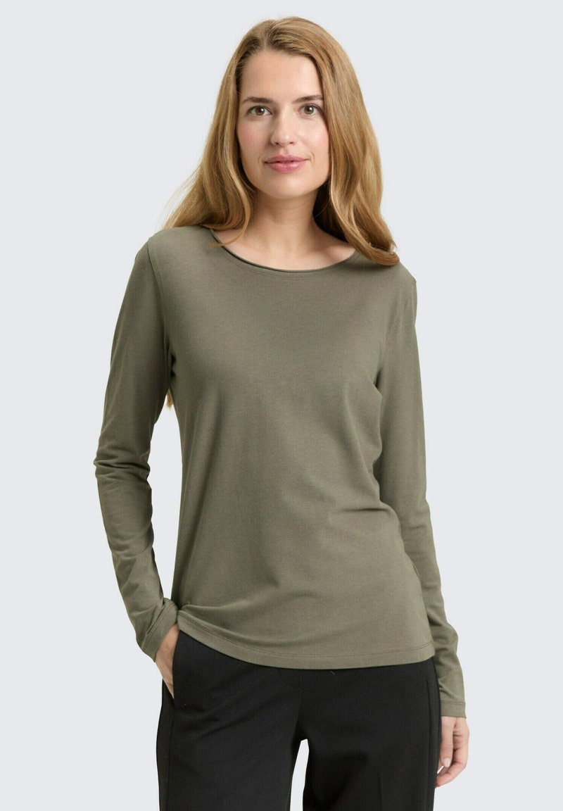 Olijfgroene longsleeve top met een ronde hals en een aansluitende pasvorm. Zachte stof en minimalistisch ontwerp, gecombineerd met een donkere broek.