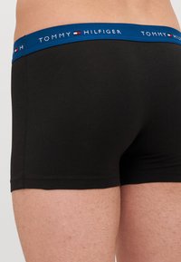 Musta bokserihousut, jotka on valmistettu puuvillasta ja joissa on sininen elastinen vyötärönauha, jossa on valkoista "TOMMY HILFIGER"-brändäystä ja logoja.