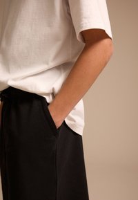 White cotton t-shirt with short sleeves, paired with black relaxed-fit pants featuring side pockets. Smooth texture, casual design.