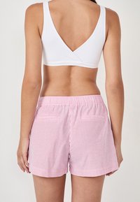 Witte, mouwloze top met een V-achterkant, gecombineerd met roze en witte gestreepte shorts met een elastische tailleband en twee achterzakken.
