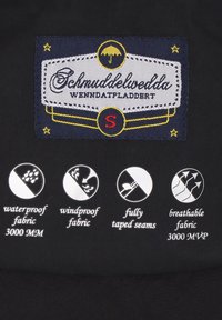 Sort stofmærkat med "Schmuddelwedda" branding. Ikoner angiver vandtæt, vindtæt, fuldt tapede sømme og åndbare stofkvaliteter.