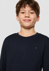 Tumesinine pika varrukaga T-särk, mis on valmistatud puuvillast, omab ümarat kaelust ja väikest logo aktsenti rinnal. Pehme tekstuur ja lihtne disain.