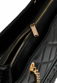 Black quilted leather handbag with gold zipper and chain detail. Features textured surface and interior compartment with smooth fabric lining.