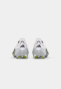 Pair of white Adidas football cleats with black stripes and green metal studs, viewed from the back on a white background.