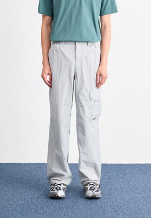 Lys grå cargobukser med en avslappet passform, med sidelommer, en glatt tekstur, og brukt med grå joggesko og en teal T-skjorte.